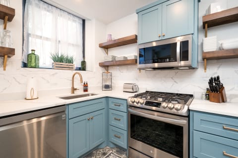 Modern kitchen featuring light blue cabinets, stainless steel appliances, and decorative elements on open shelves.