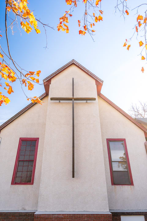 Exterior view of a church with a cross, framed by autumn leaves.