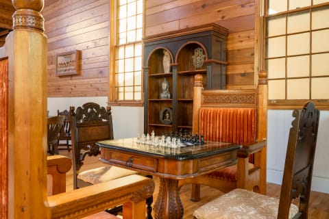 An intricately designed chess table with black and white pieces in a wooden room with large windows.