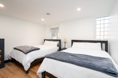A bright bedroom with two beds, a dresser, and warm lighting.
