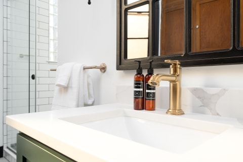 Modern bathroom with a white sink, gold faucet, and dark amber toiletry bottles.