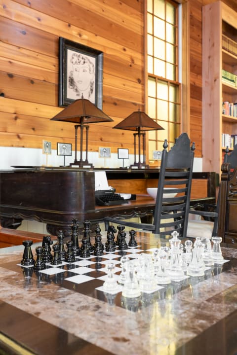 A chessboard with black and clear pieces in a room with wooden walls and a typewriter.