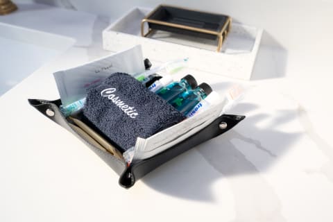 A black leather cosmetic pouch containing toiletries and a towel on a marble surface.