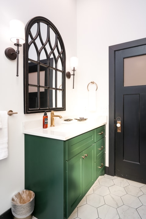 Modern bathroom with green vanity, arched mirror, and stylish fixtures.