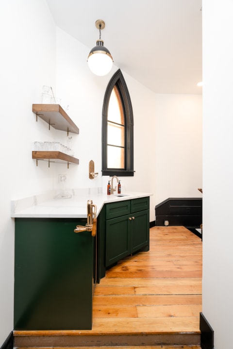 Interior view of a small bar area featuring green cabinets, a white countertop, and an arched window.