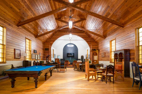 Interior of a room with a pool table, antique chairs, and a vaulted wooden ceiling.