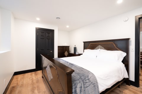 A modern bedroom with a dark wooden bed, white bedding, and light wood flooring.