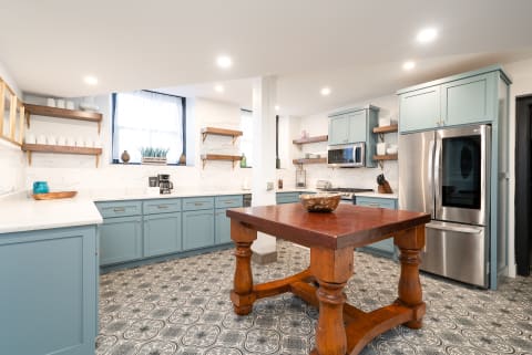 A modern kitchen featuring blue cabinets, a wooden table, and patterned tiled flooring.