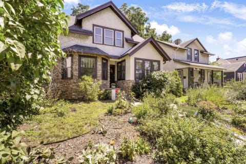 Craftsman-style house with stone foundation and thriving gardens in a serene neighborhood.