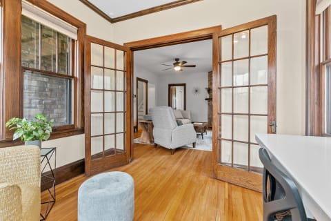 Sunroom with hardwood floors, French doors, a cozy ottoman, and a view into a stylish living room.