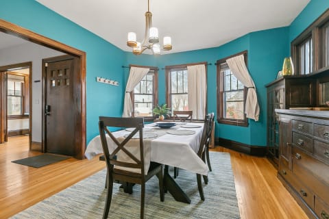 Bright dining room featuring turquoise walls, wooden furniture, and large windows with soft curtains.
