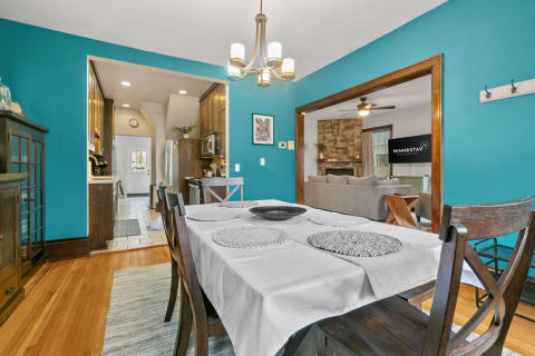 A dining area with a turquoise wall, wooden table, and a cozy living room visible in the background.