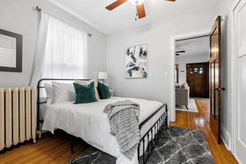 A serene bedroom with a bed dressed in white linens and emerald green pillows, featuring a vintage radiator and wooden flooring.