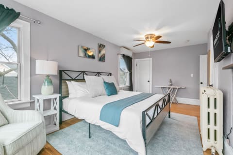 A serene bedroom with light gray walls, a metal bed frame dressed in white bedding, and a turquoise throw blanket, complemented by stylish decor.