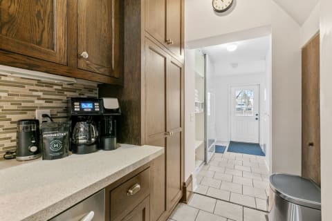 A kitchen featuring wooden cabinets and a coffee maker, leading to a bright hallway and entrance.