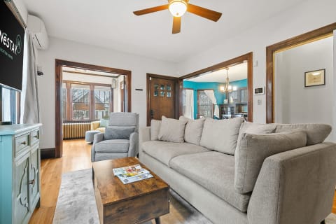 A spacious living room with gray sofas, hardwood floors, and an open layout to a dining area with a blue wall.
