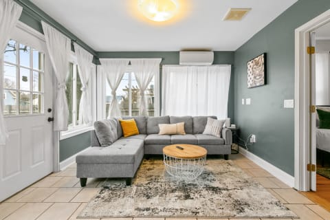 Cozy living room with gray sectional sofa, light wooden coffee table, and large windows with white curtains.