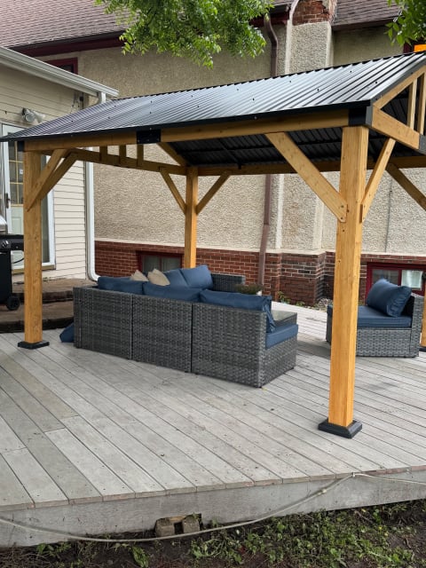 Outdoor gazebo with wicker seating and blue cushions on a wooden deck.