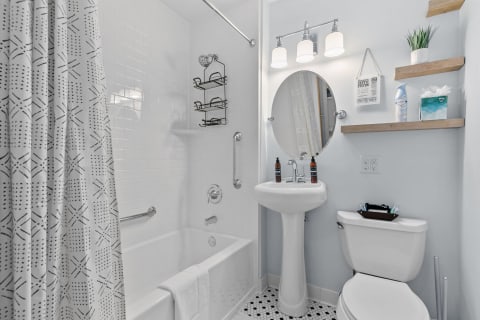 A modern bathroom featuring a soaking tub, pedestal sink, decorative shelves, and contemporary lighting.