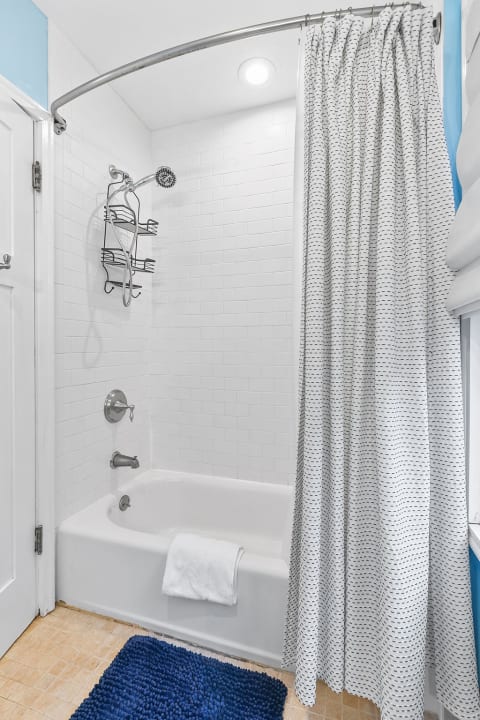 A clean, modern bathroom featuring a tub-shower combo, a curved shower rod, and neatly arranged towels on a rack.