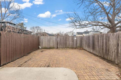 Private brick patio enclosed by wooden fencing, with bare trees and a blue sky above.