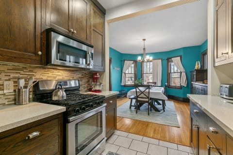 A modern kitchen with dark wood cabinets and appliances, leading into a bright dining area with turquoise walls.