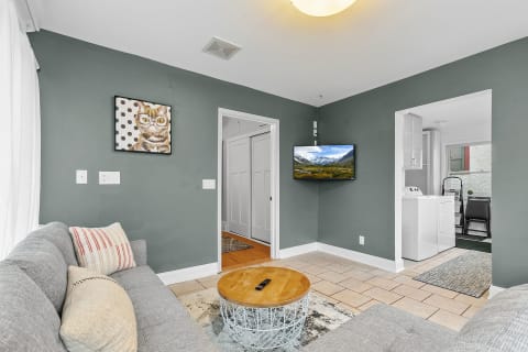 Cozy living room featuring gray sofas, a cat artwork, and a television displaying a mountain scene.