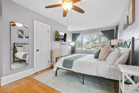 Serene bedroom with lavender walls, a cozy bed, large windows, and stylish decor.