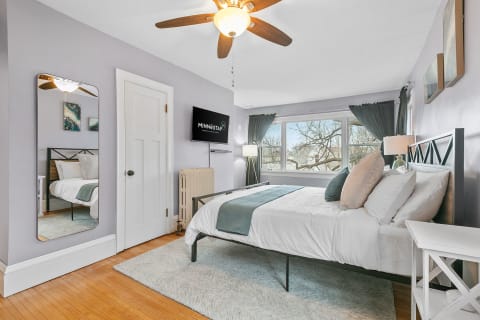 A cozy bedroom featuring a metal bed frame, natural light from large windows, and stylish decor.