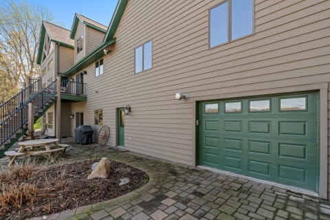 Exterior view of a large beige house with green accents and a picnic table.