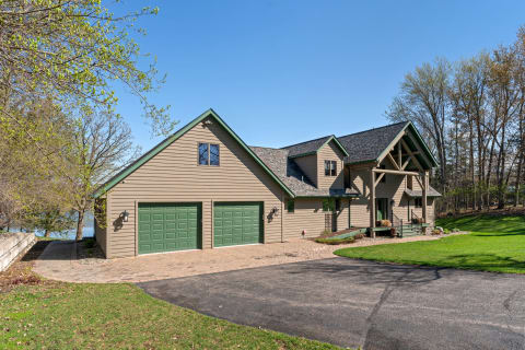 A modern house with green garage doors and tan siding, nestled amongst trees by the water.