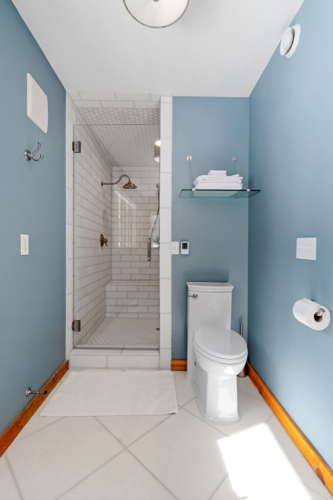 Modern bathroom with blue walls, a glass shower, and white fixtures.
