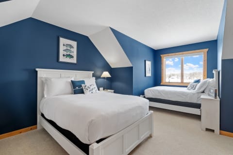 Cozy bedroom with a large bed and daybed, decorated in blue tones and illuminated by natural light from a window.