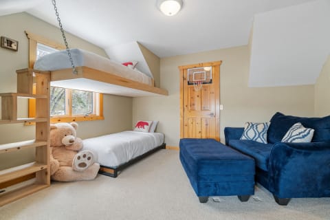 A cozy children's room with a loft bed, plush teddy bear, and blue couch.