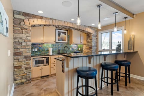 A stylish kitchen featuring a stone archway, vibrant tiled backsplash, and dark granite countertops with bar stools.