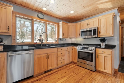 A wooden kitchen featuring granite countertops, stainless steel appliances, and large windows with a snowy outside view.