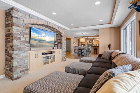 Cozy living room featuring a sectional couch and a large flat-screen TV on a stone wall.