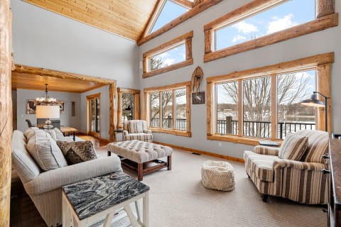 A spacious living room featuring high wooden ceilings, large windows, and rustic furniture.
