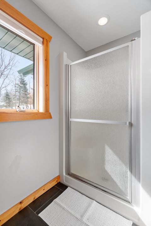 Bright bathroom corner showing a frosted glass shower and wooden-framed window.