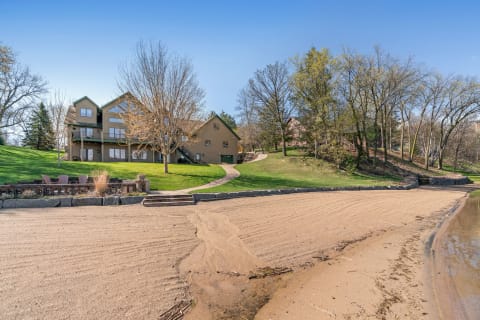 A sandy beach in front of a house surrounded by trees and a clear blue sky.