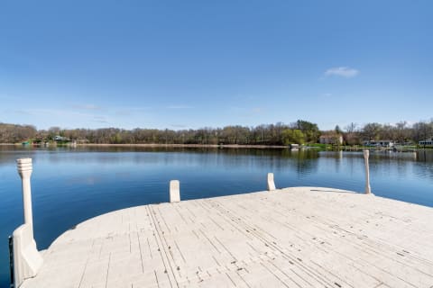 View of a calm lake from a white dock under a clear blue sky.