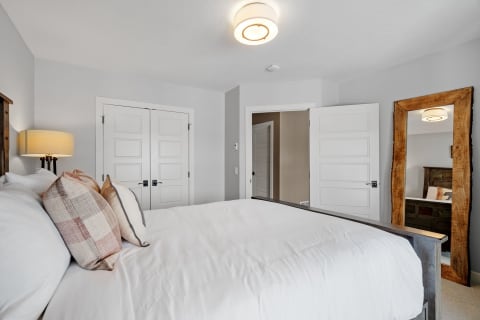 Modern bedroom with a large bed, stylish pillows, and a wooden mirror.
