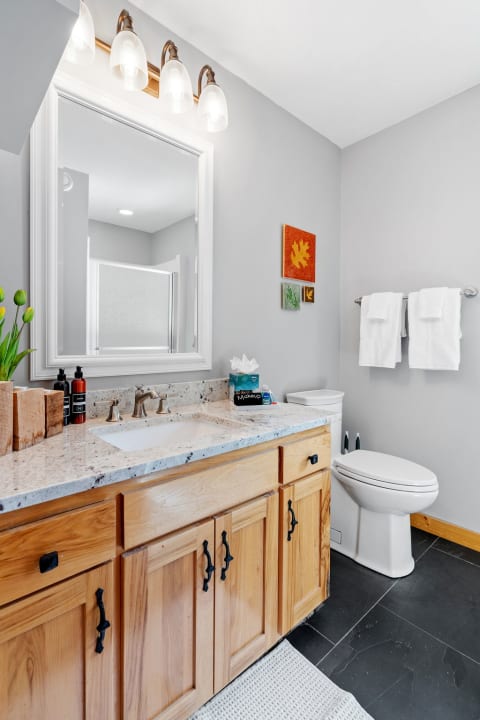 A bright bathroom featuring a granite countertop, wooden cabinets, and colorful wall art.
