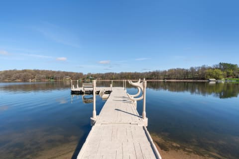 A long dock leading into a tranquil lake with surrounding trees and homes.