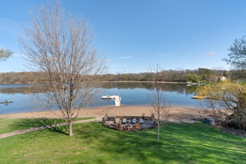 A peaceful lakeside scene with a fire pit and sandy beach under a blue sky.