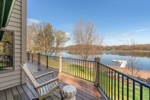Lakeside view from a deck featuring a wooden chair and a boat dock in the distance.