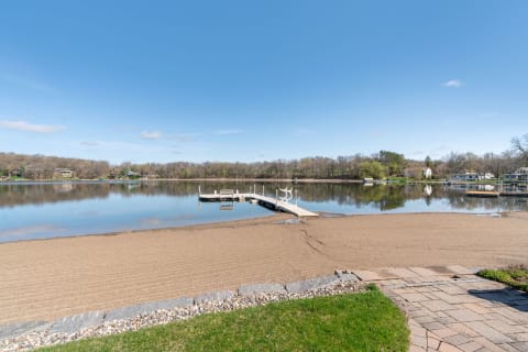 Lakeside scene with a sandy beach, wooden dock, and clear blue sky.