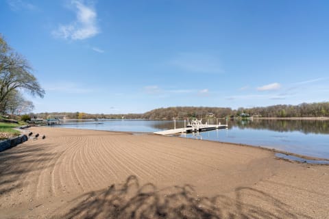 Serene lakeside view with sand patterns and a dock under a clear sky.