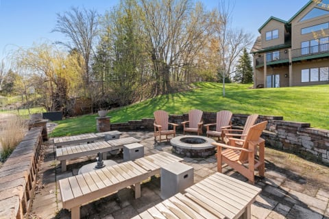 Outdoor patio featuring a firepit, wooden chairs, and a serene lawn in spring.