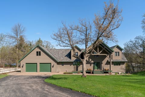 A two-story house with brown siding, green trim, and a spacious lawn.